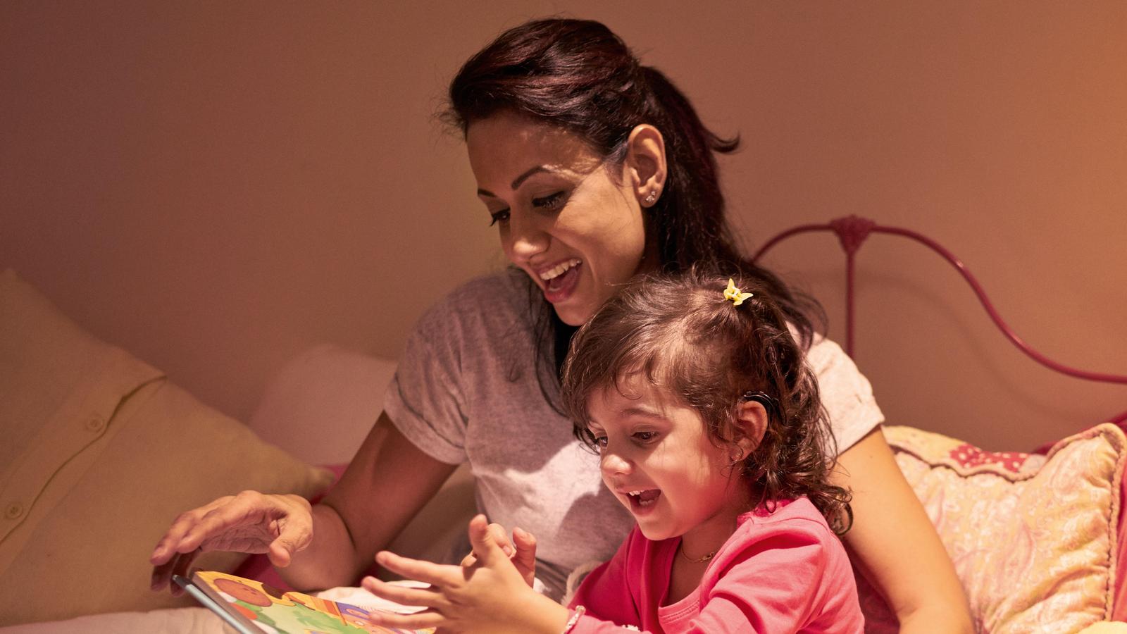 Ett barn med implantat lyssnar på sin mamma som läser en bok