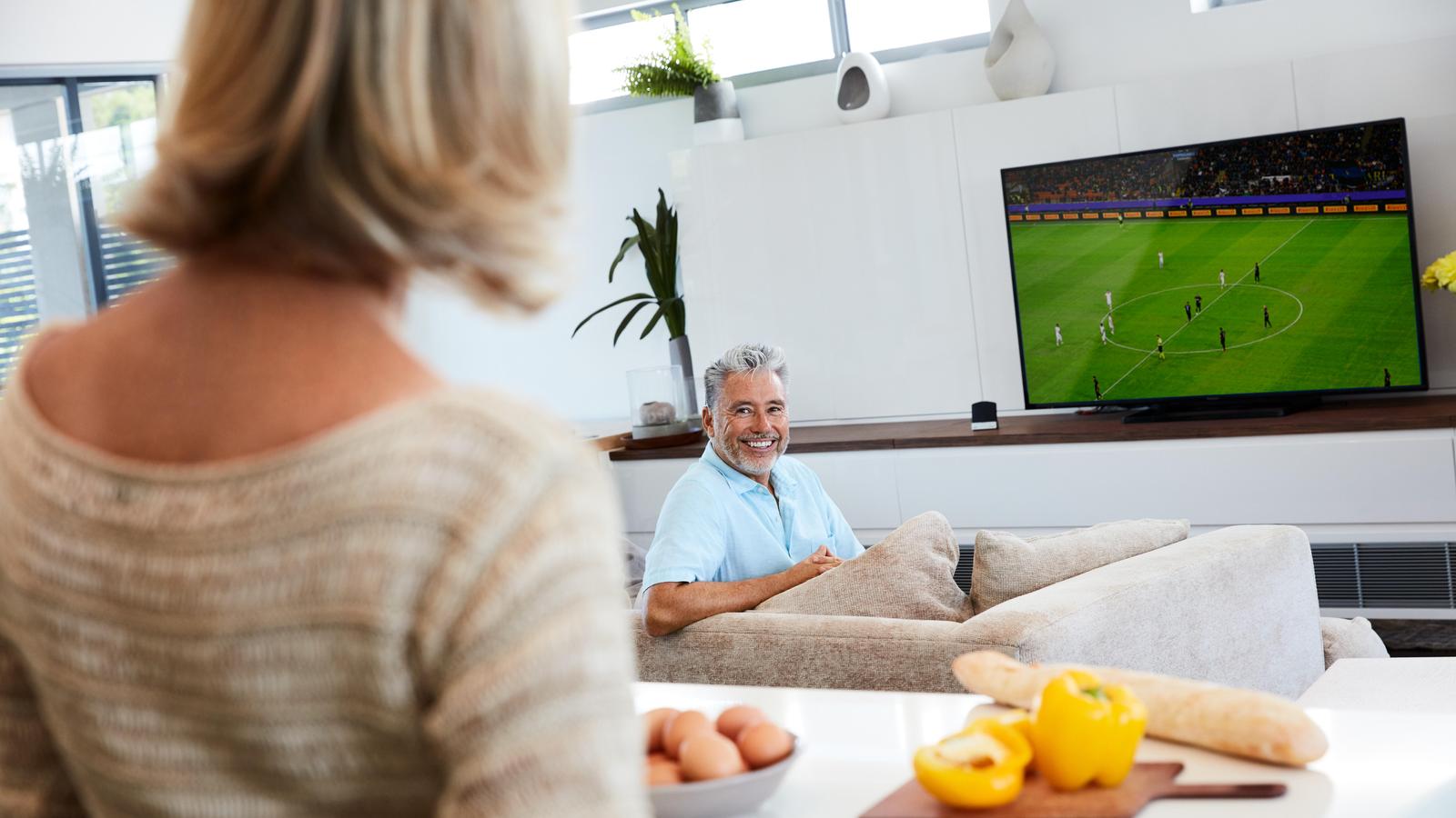 Un homme regarde le football à la télévision avec le Cochlear Wireless TV Streamer (émetteur audio TV)