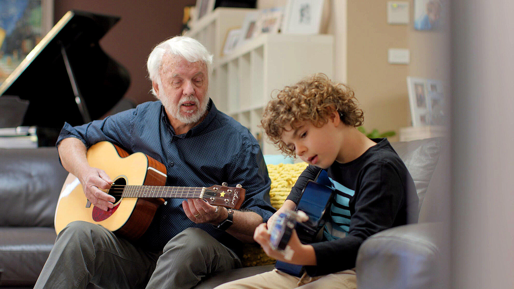 Ein Mann und ein Kind, das ein Cochlea-Implantat trägt, spielen Akustikgitarre