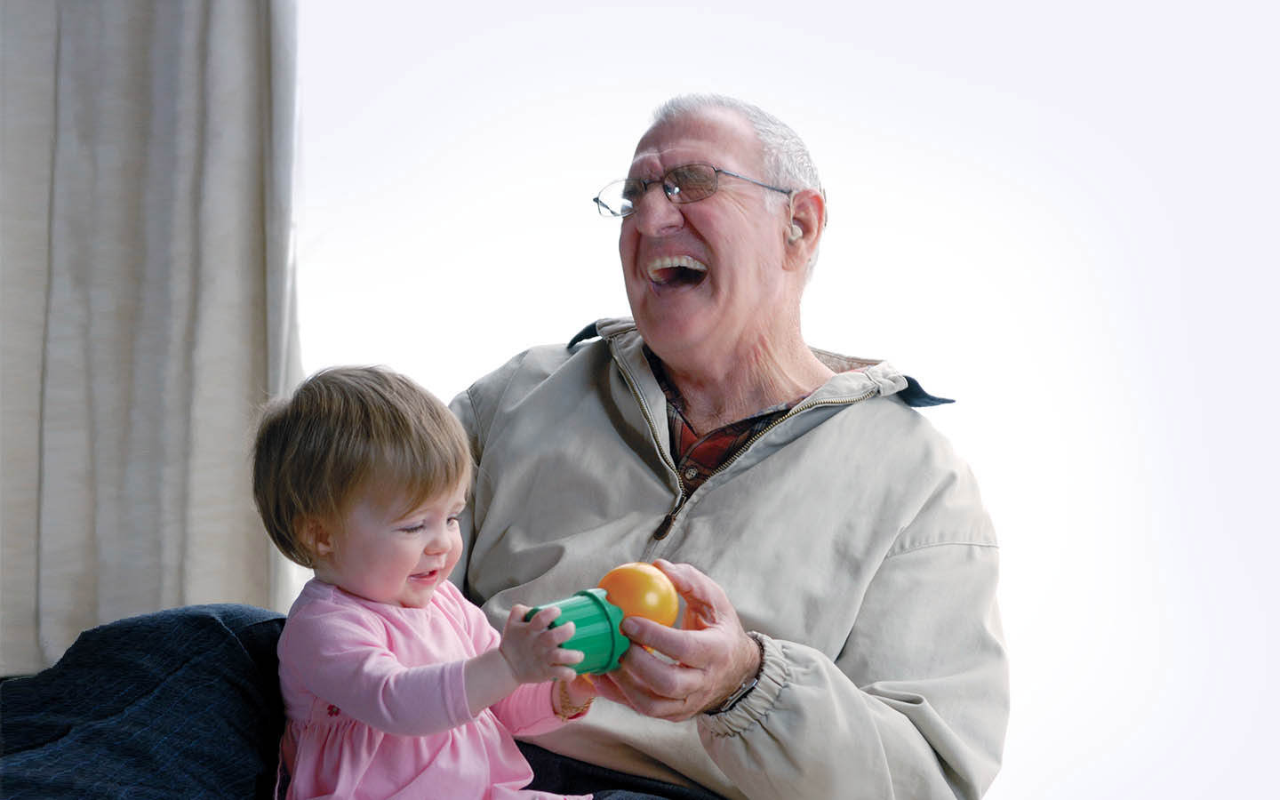 An elderly implant recipient laughs as his grandchild sits on his lap