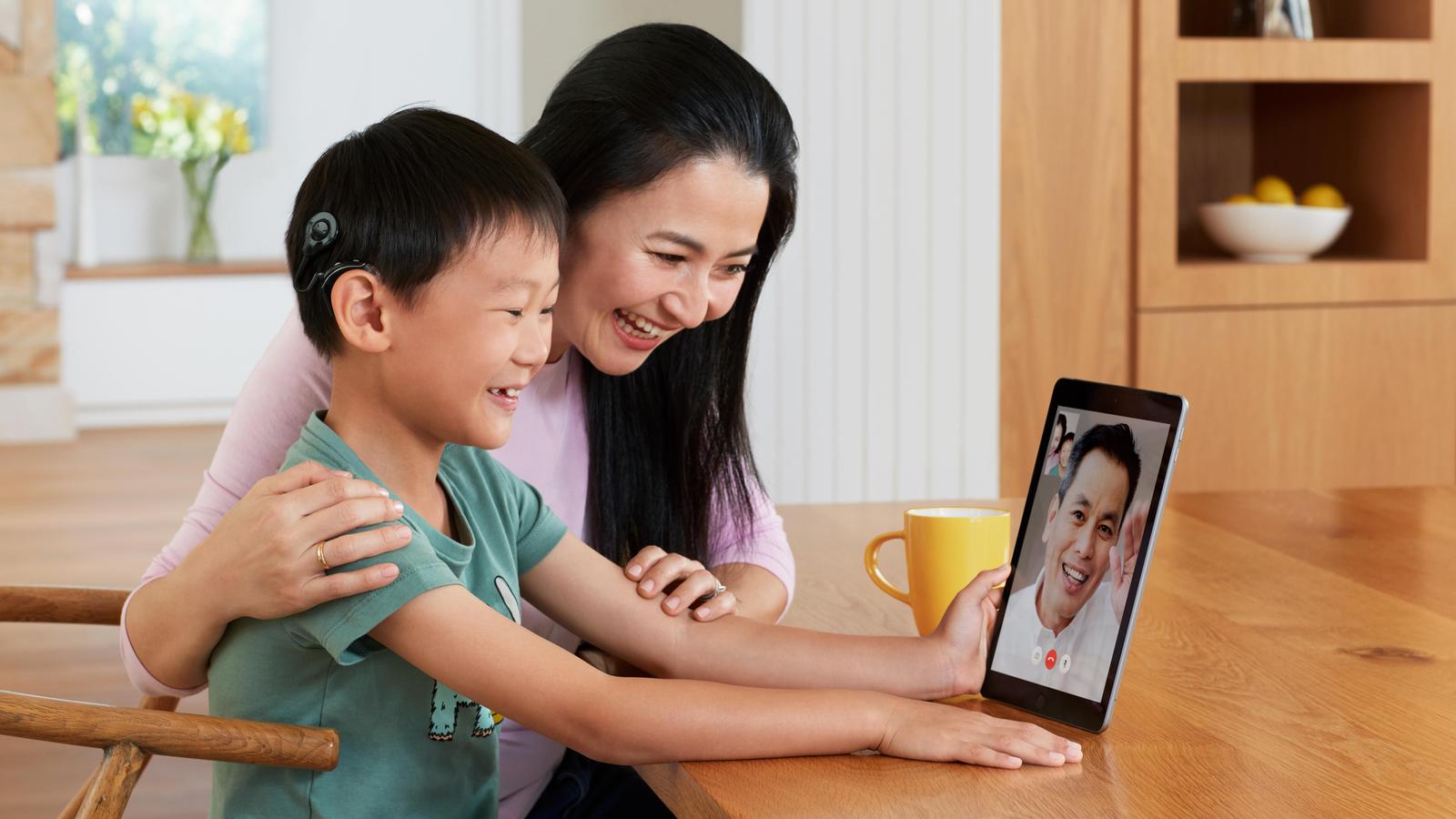 Niño asiático con procesador de sonido Nucleus habla con su padre por FaceTime