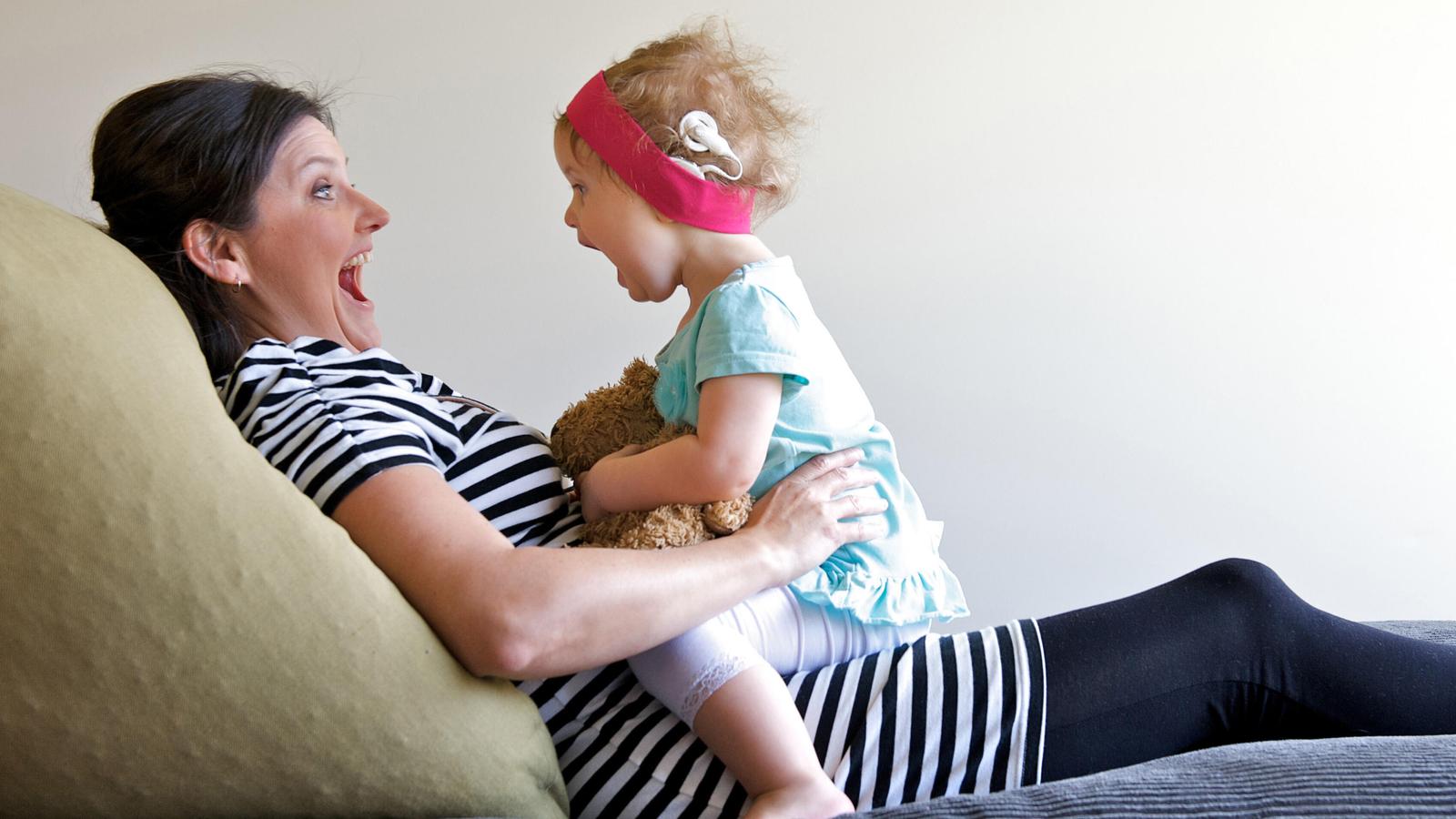 Ein Kleinkind, das ein Implantat trägt, sitzt lachend auf dem Schoss seiner Mutter
