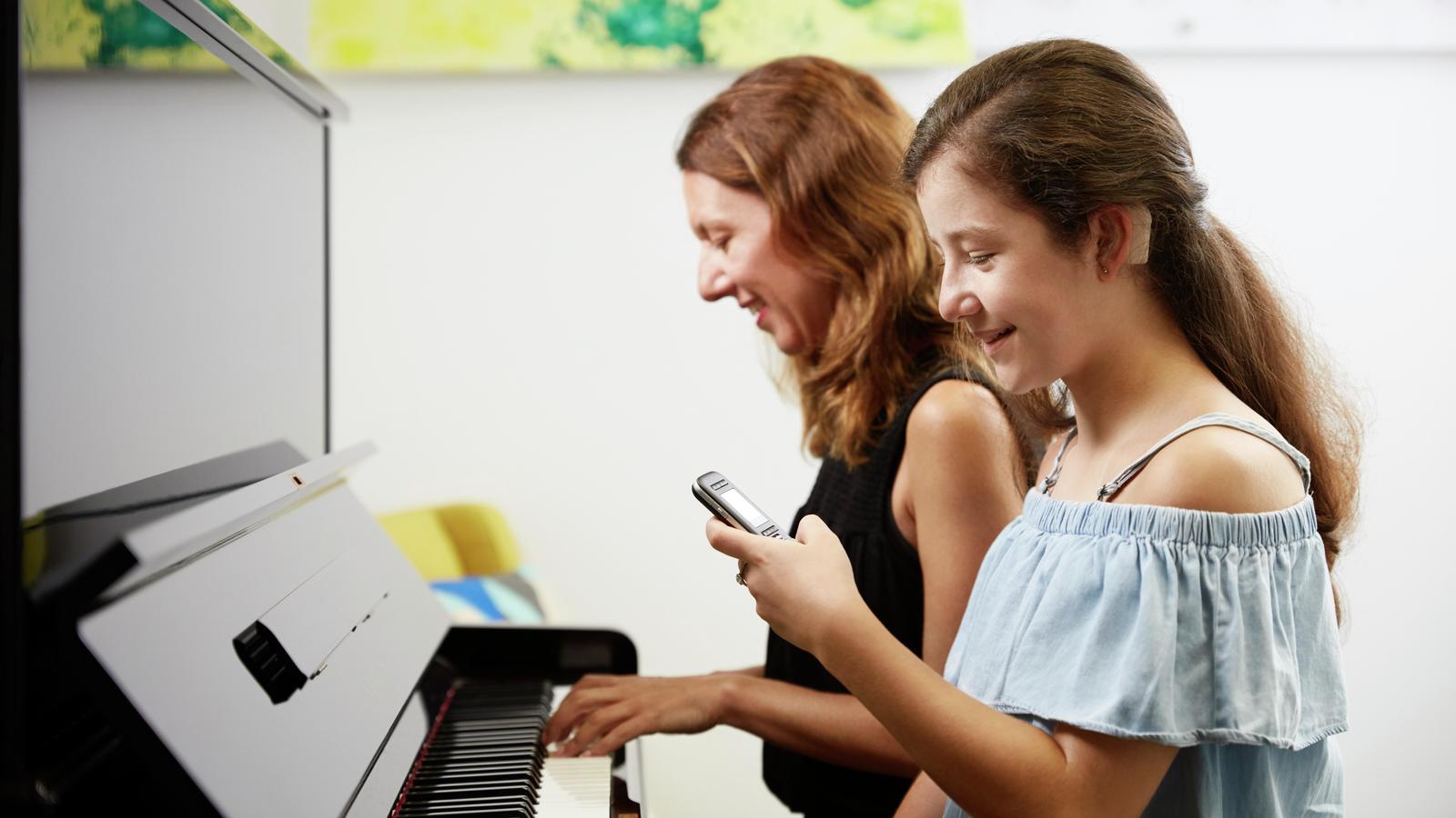 Tonårstjej använder mikrofon medan hennes mamma spelar piano