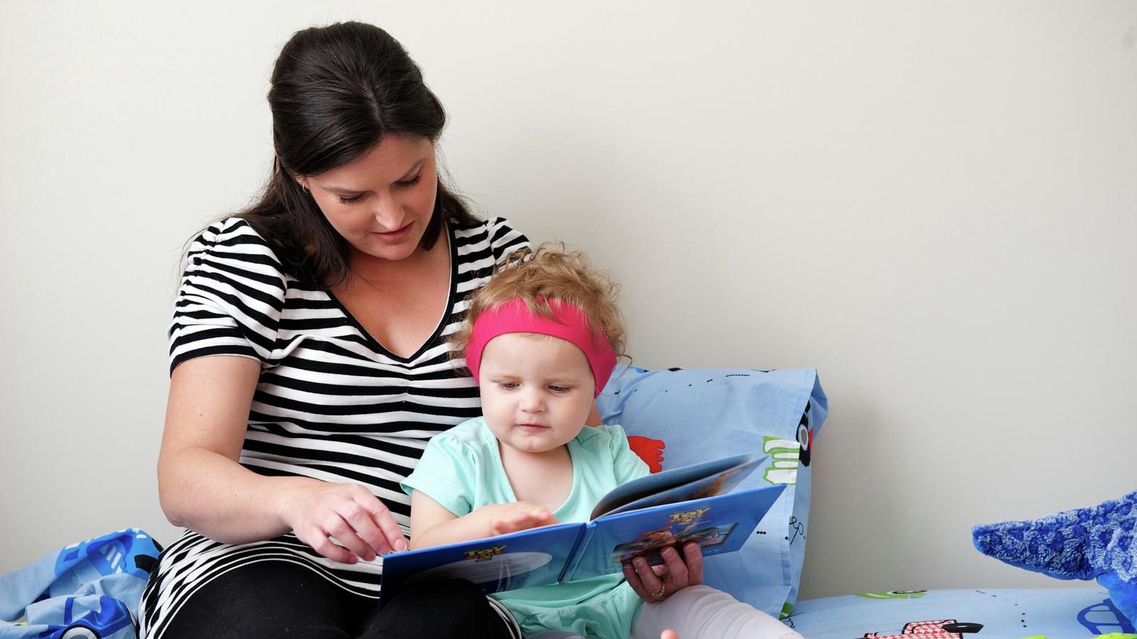 A woman reads a book to a child wearing a hearing device
