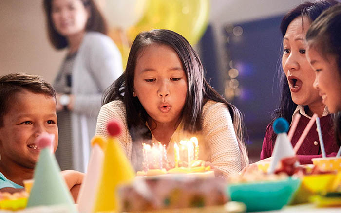 Ragazza con impianto Cochlear che soffia sulle candeline della sua torta di compleanno con la famiglia